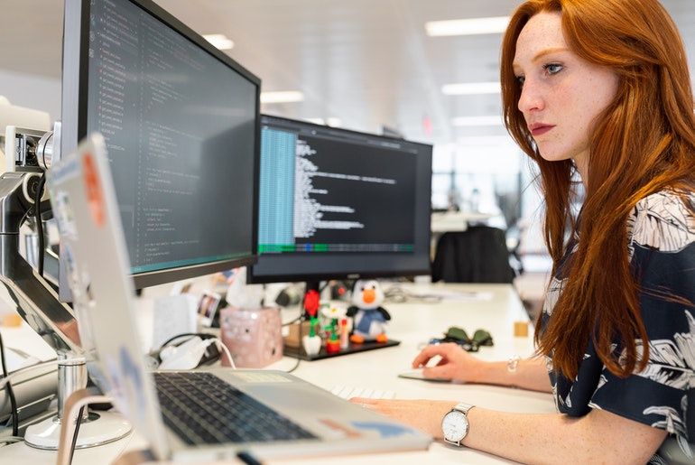 Woman with dual monitors coding
