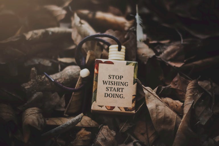 A small tag on leaves with the phrase "Stop Wishing Start Doing" written on it
