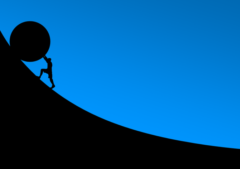 Silhouette of man pushing ball up a hill
