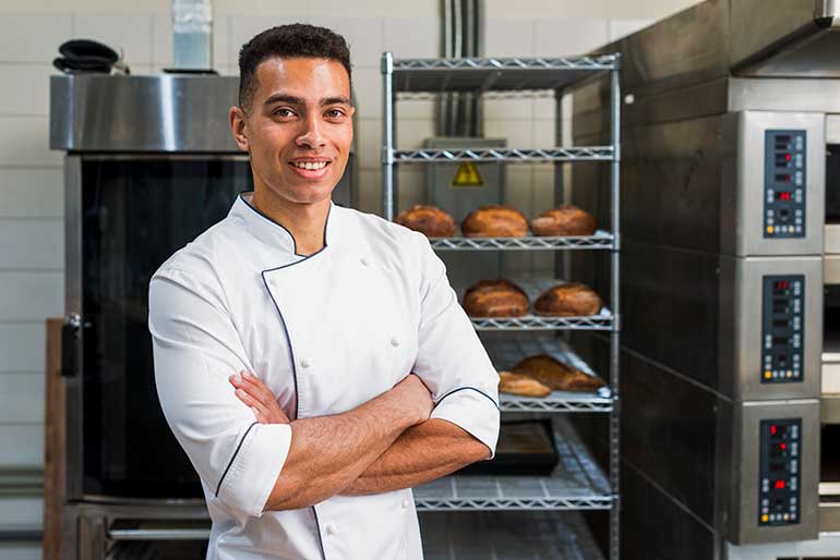 Young male baker standing in front of bread