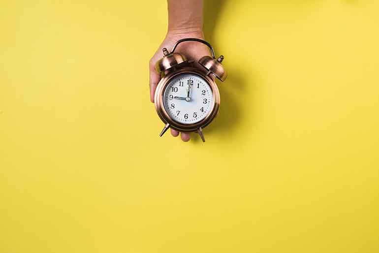 Hand holding a brass alarm clock on yellow background