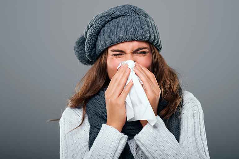 Woman wearing winter closthing sneezing into a tissue