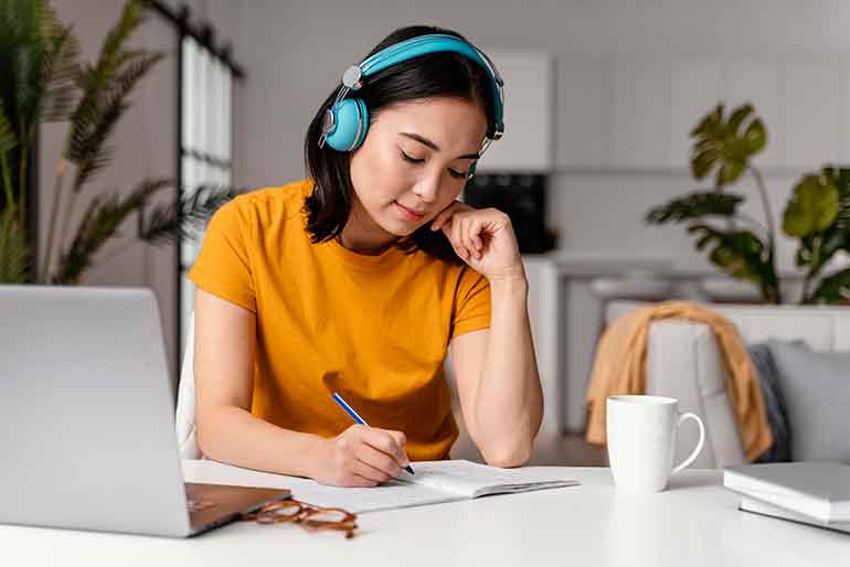 Woman wearing headphones and taking notes