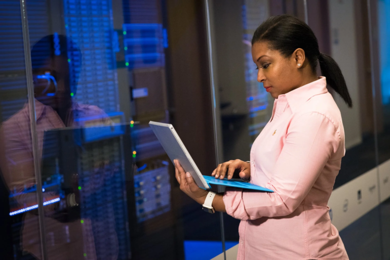 Woman looking at laptop standing in front of a server bank