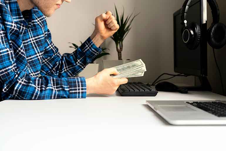 Man working at a laptop holding cash