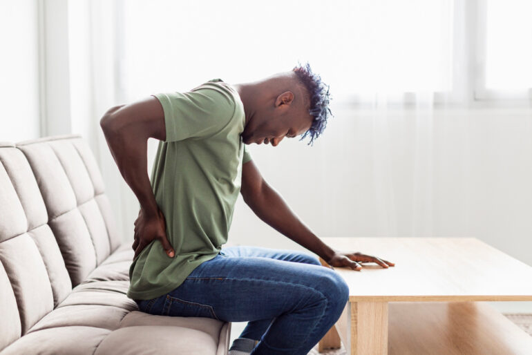 Man sitting on a sofa in pain, rubbing his back