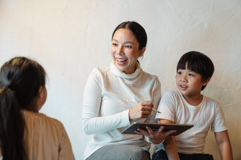 Smiling woman holding a tablet and teaching two children