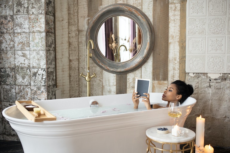 Woman reading in a bath under a large mirror