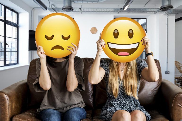 Two people holding a happy and sad emoji