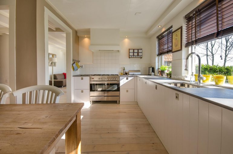 Brightly lit kitchen with white cupboards and a wooden floor