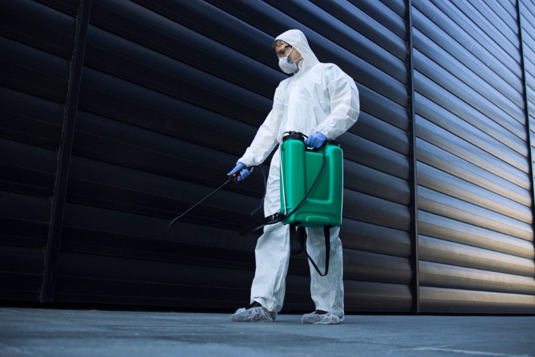 Person spraying chemicals while wearing a chemical protection suit