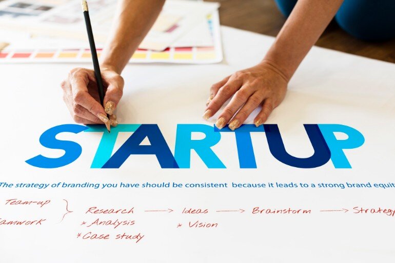 The word startup on a large piece of paper with someone writing with a pencil