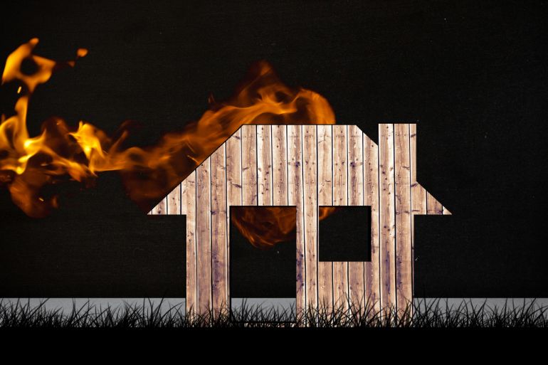 Wooden cutout in the shape of a house with flames coming from the roof