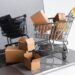 Model of a shopping cart filled with packages sitting on a laptop keyboard