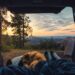Two people lying in the back of a camper van looking out over woodland