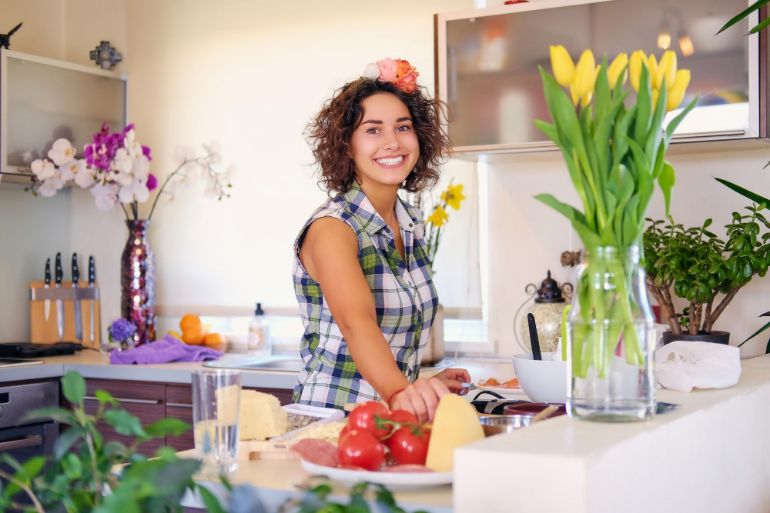 Smiling woman In a kitchen surrounded by produce and spring flowers
