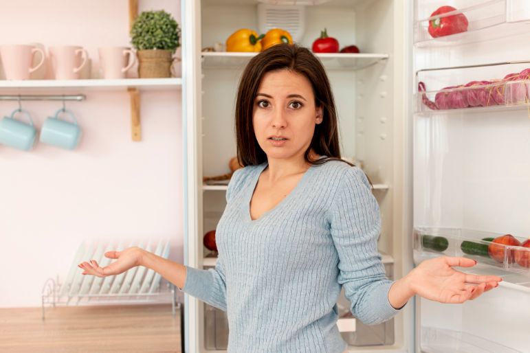 A woman standing in front of an open fridge looking confused