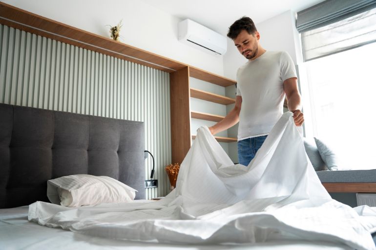 Man holding a sheet while changing the bed