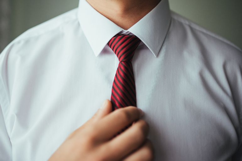 Person wearing a white shirt and straightening a red and black striped tie