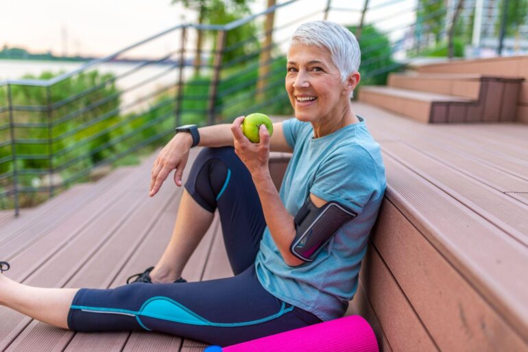 Woman wearing fitness gear sitting on decking while eating an apple