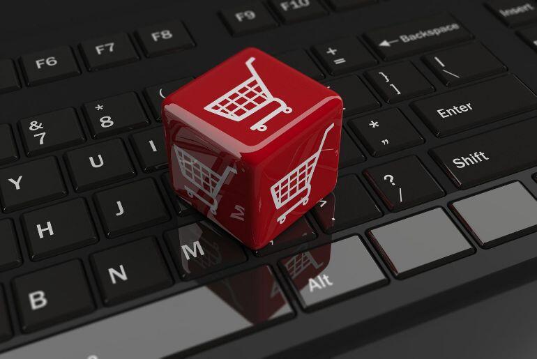 A red cube with an image of a white shopping cart on each face sitting on the keyboard of a laptop