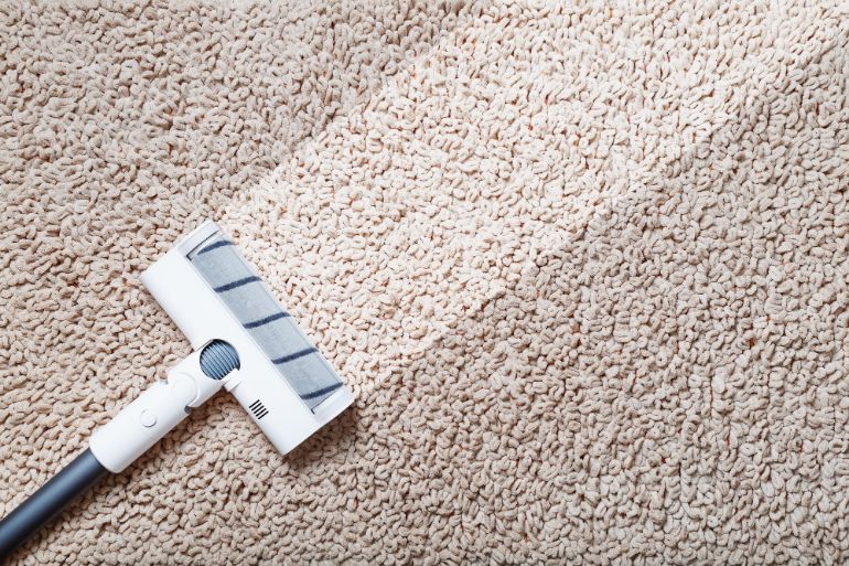 A white and grey vacuum being run over a beige carpet