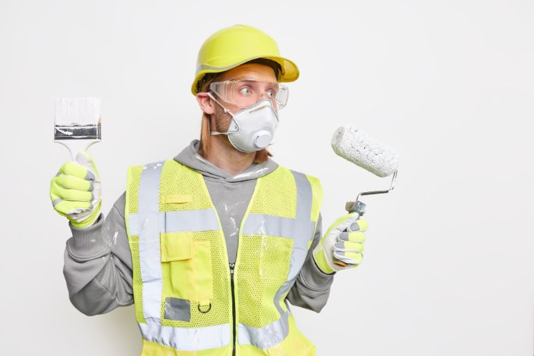 Person wearing safety gear while holding a paint brush and roller