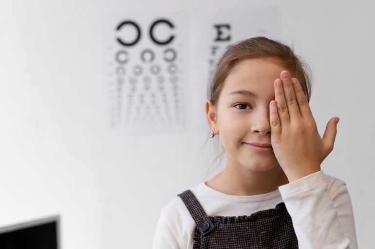 Small child covering one eye sitting in front of an optometrists eye chart