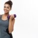 Smiling woman in athletics gear holding two purple dumb bells