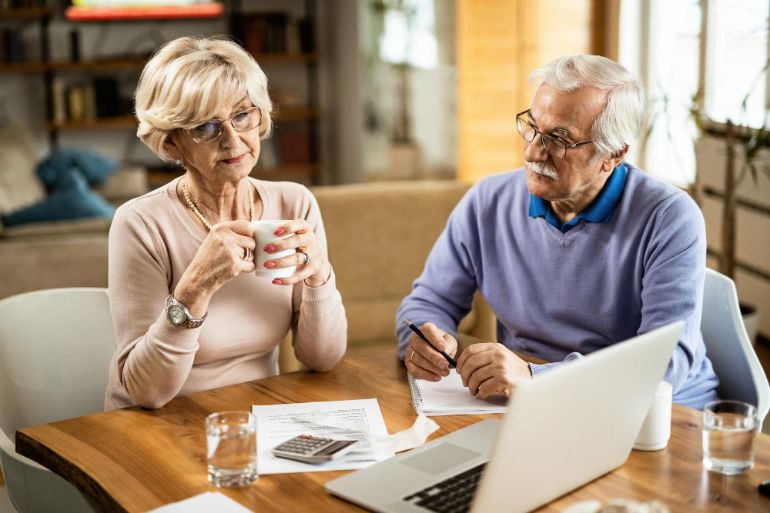 An older couple sat at a dining table looking at financial paperwork