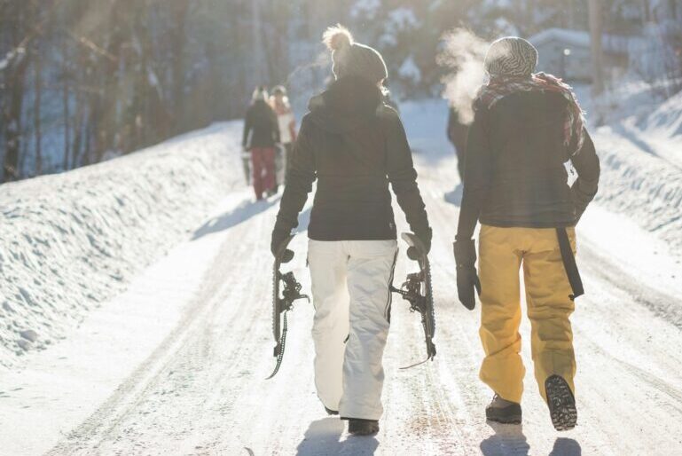 A couple of people walking on a snowy road holding skis