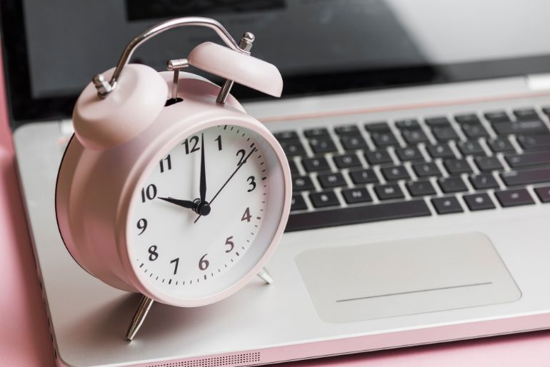 A pink analogue alarm clock sitting on a laptop keyboard