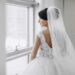 Bride wearing a white dress and veil standing in front of a window