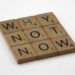 Wooden blocks saying "Why Not Now" on a white surface