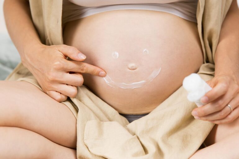 A person making a smiling face out of body lotion on their baby bump