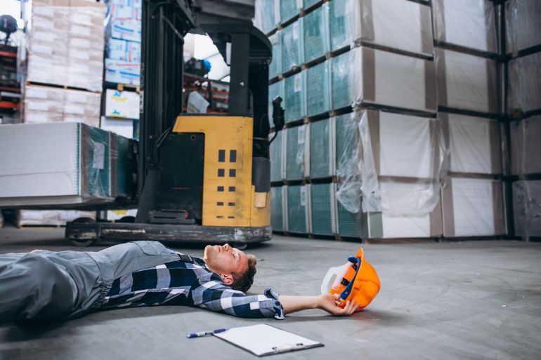 Man laying on the floor in front of a forklift truck