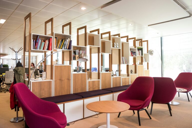 An open plan office with a comfortable seating area separated from workers by boxed shelving