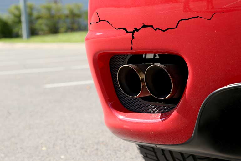 Red car bumper with dual exhaust pipes with a large crack running across the top of the bumper