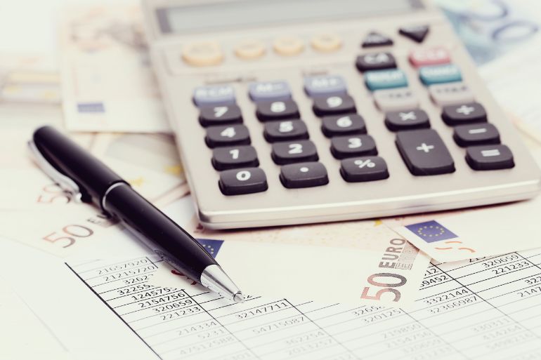 A calculator and pen sitting on a pile of bank notes