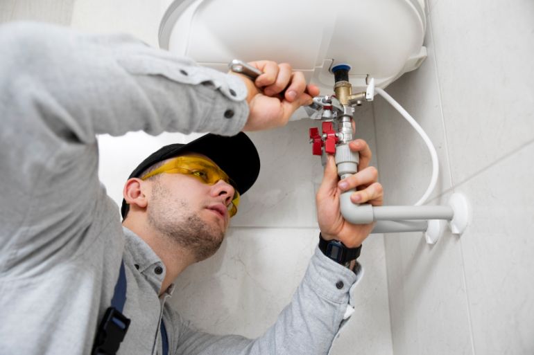 A person working on pipes under a small sink