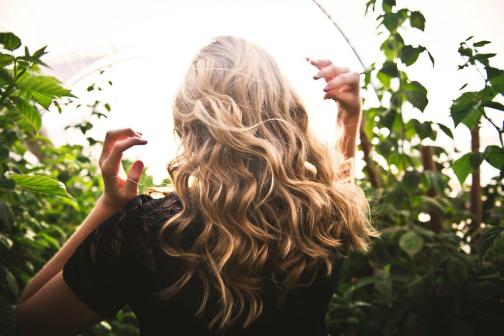 A woman with long blonde hair walking through tall green plants